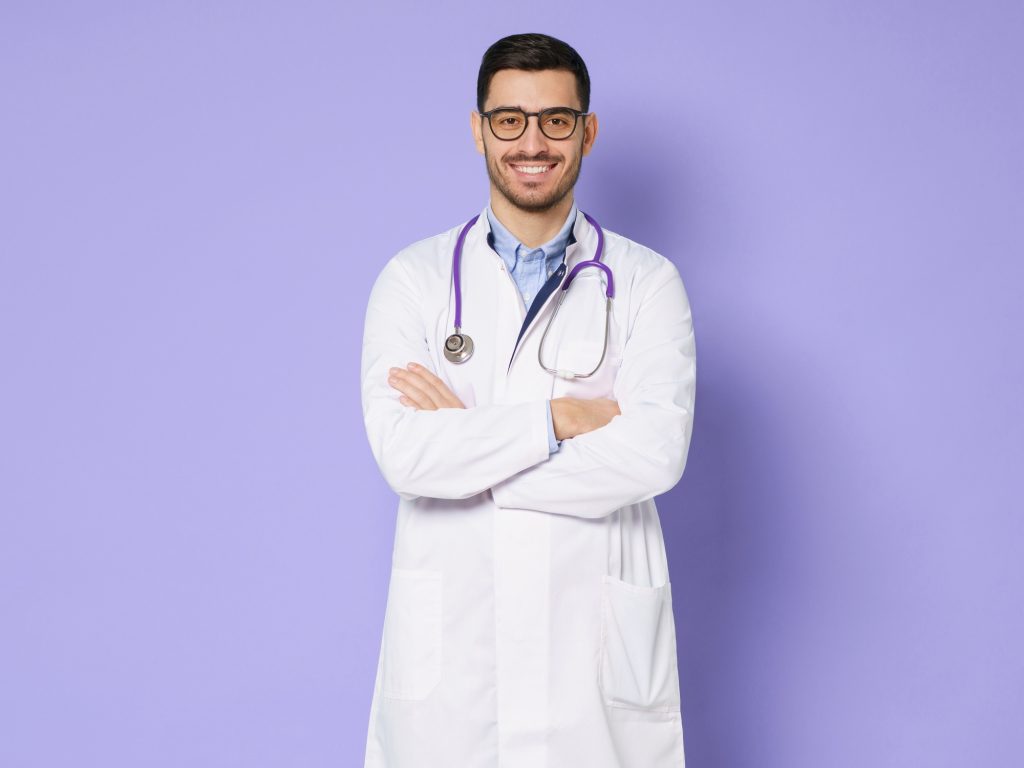 Young male doctor standing with arms crossed, wearing white doctor robe with stethoscope